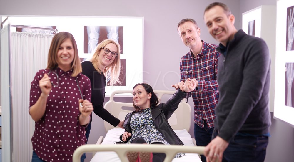 person lying on hospital bed and 3 people standing around her taking her blood pressure
